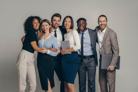 Smiling young business team in formalwear embracing while standing on beige backgroundの写真素材