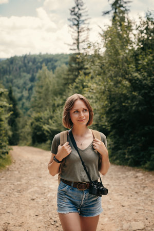 Smiling young female traveler with backpack walking by the mountain footpathの写真素材