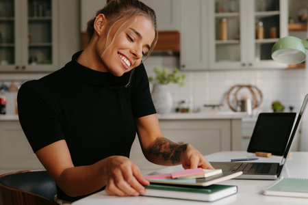 Busy young woman talking on mobile phone and smiling while working at homeの写真素材