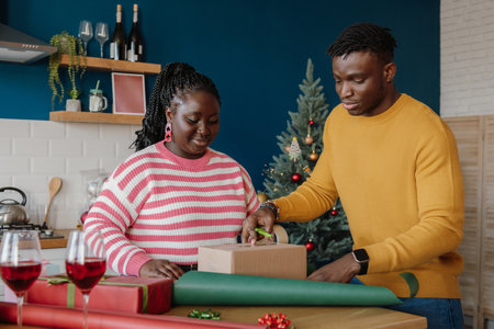 Beautiful young African couple wrapping Christmas gifts in colorful paper at home togetherの写真素材