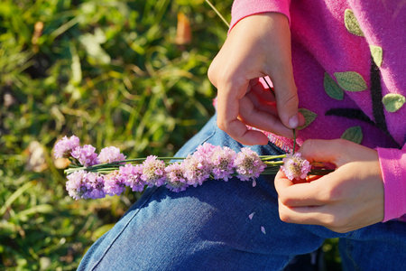 the child's hands weave a wreath of purple flowers.の写真素材