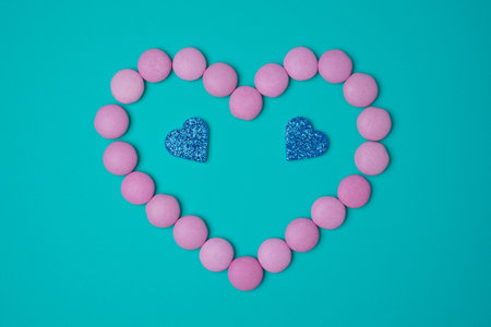 Pink sweets candies as heart with two glittering blue hearts on blue green turkuoise background. Valentines day concept. flat lay.の写真素材