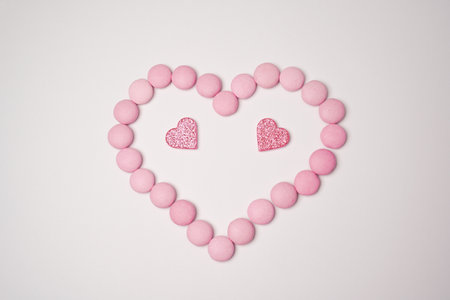 Sweets candies as heart with two glittering pink hearts on white background. Valentines day concept. flat lay.の写真素材