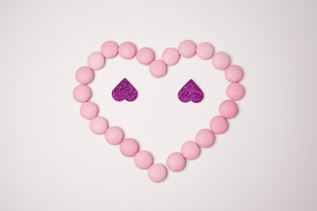 Sweets candies as heart with two glittering lilac hearts on white background. Valentines day concept. flat lay.の写真素材