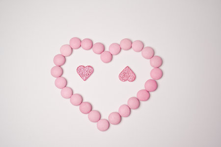 Sweets candies as heart with two glittering pink hearts on white background. Valentines day concept. flat lay.の写真素材