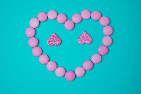 Sweets candies as heart with two glittering pink hearts on blue green turkuoise background. Valentines day concept. flat lay.の写真素材