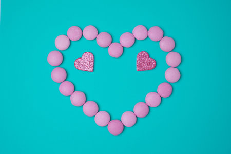 Sweets candies as heart with two glittering pink hearts on blue green turkuoise background. Valentines day concept. flat lay.の写真素材
