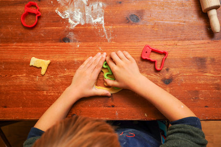 Hands of a toddler child cutting shaped biscuits out of dough on a brown wooden tabel. Christmas baking.の写真素材