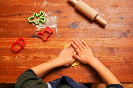 Hands of a toddler child cutting shaped biscuits out of dough on a brown wooden tabel. Christmas baking.の写真素材