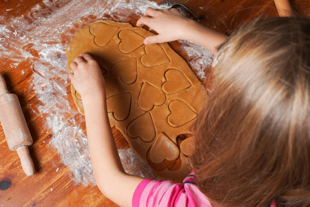 Hands of child makes biscuits, cookies as hearts out of dough. Rolling pin on a table. Valentine's Day celebration.の写真素材
