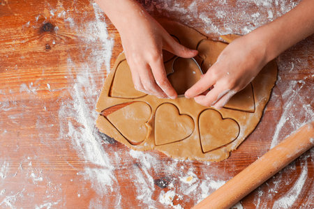 Hands of child makes biscuits cookies as hearts out of dough. Rolling pin and flour on a table. Valentine's Day celebration.の写真素材