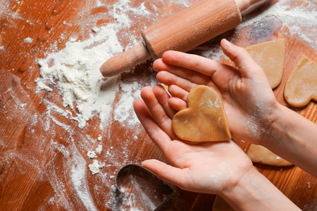 Biscuit, cookie as heart out of dough on hands of child . Heart molds, rolling pin and flour on a table. Valentine's Day celebration.の写真素材