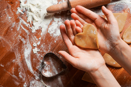 Biscuit, cookie as heart out of dough on hands of child . Heart molds, rolling pin and flour on a table. Valentine's Day celebration.の写真素材