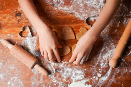 Hands of child makes biscuits cookies as hearts out of dough. Heart molds, rolling pin and flour on a table. Valentine's Day celebration.の写真素材