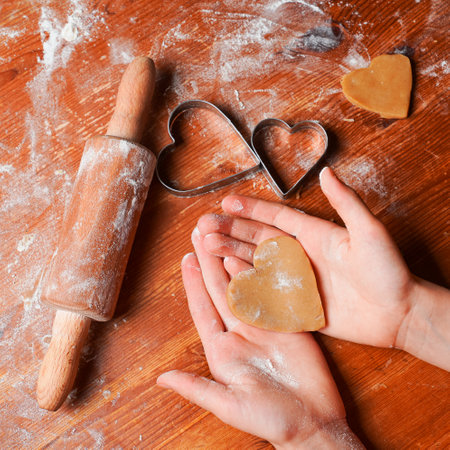 Biscuit, cookie as heart out of dough on hands of child . Heart molds, rolling pin and flour on a table. Valentine's Day celebration.の写真素材