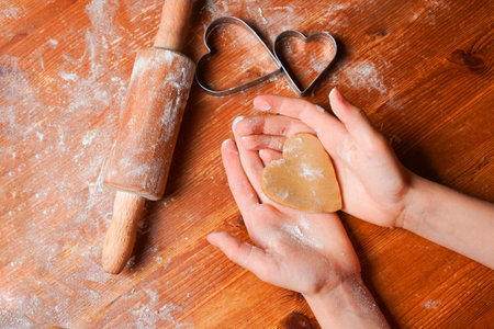 Biscuit, cookie as heart out of dough on hands of child . Heart molds, rolling pin and flour on a table. Valentine's Day celebration.の写真素材