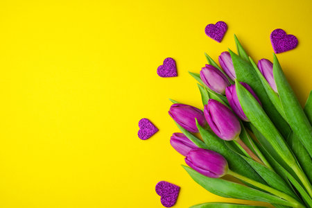 Bouquet of purple tulips with hearts on yellow background. Mothers day, Valentines Day, Birthday celebration concept. greeting card. Copy space, top view.の写真素材