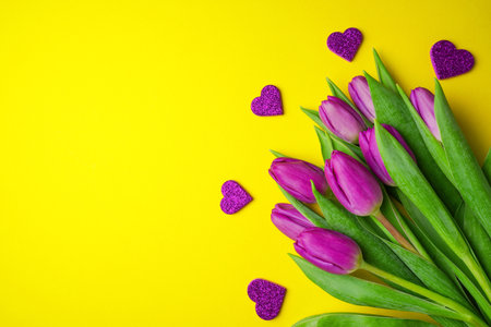 Bouquet of purple tulips with hearts on yellow background. Mothers day, Valentines Day, Birthday celebration concept. greeting card. Copy space, top view.の写真素材