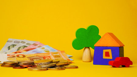 Euro cash money euro coins and banknotes with wood toy house, tree and auto on yellow background. Property Ownership Concept.の写真素材