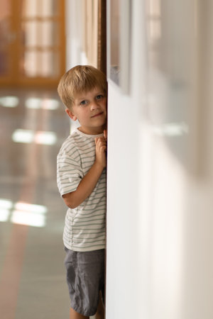 Boy playing hide and seek in corridor, Active kid looking out while hiding behind the white wall, Positive kid.の写真素材
