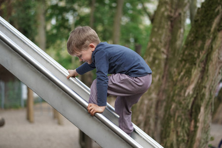 Little Boy trying to go up the slider. Preschool child playing outdoor playground. Happy toddler child climbing and having fun with summer outdoors activityの写真素材