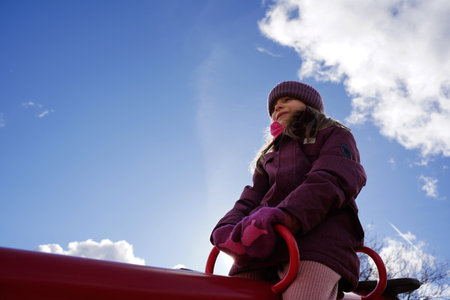 Little girl playing on outdoor playground. Happy child having fun on a swing. Outdoors activity. Blue sky backgroundの写真素材