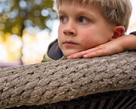 Close up portrait of little sad kid lying on round nest swing on autumm day in park. Loneliness. one child in the family.の写真素材