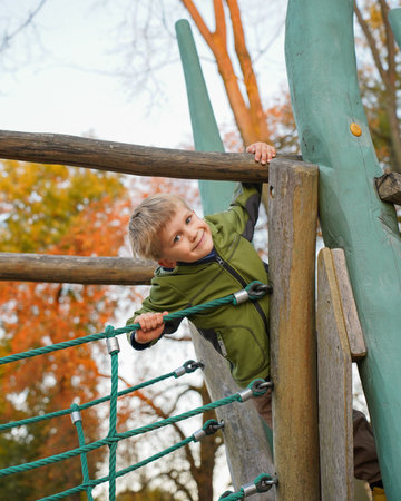 Portrait of happy smiling boy in yellow jacket on a playground , view from bottom up, autumm, copy space.の写真素材