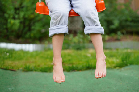 Children's legs hanging from the swing. Closeup of happy kid sitting and swinging, sunny summer day, countryside background. child feet barefoot.の写真素材
