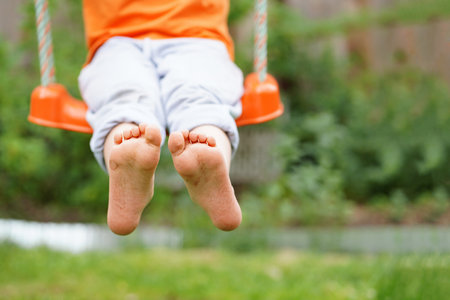 Closeup of happy kid sitting and swinging, sunny summer day, countryside background. child feet barefoot. copyspace.の写真素材