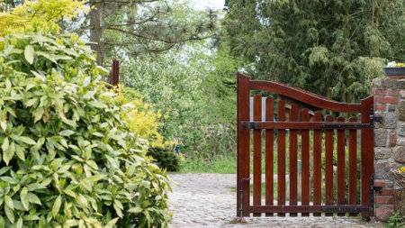 Beautiful brown wooden gates in a green garden, one part slightly open, inviting you inside.の写真素材