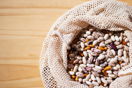 Variety of speckled beans in crocheted reusable bag on wooden surface. Zero waste lifestyle. Healthy eating and plant-based nutrition. International Year of Pulses. World Food Day. Vegan and vegetarian dietsの写真素材