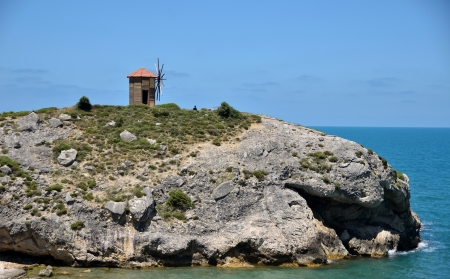 Giant rock is near sea with a windmill on it の写真素材