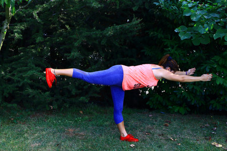 Yoga instructor shows virabhadrasana, warrior pose on green grasses.