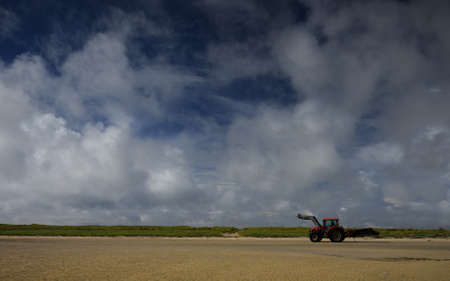 A Red tractor being driven on the beach at North Uist in the Outer Hebridesの写真素材