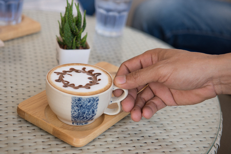 hand holding hot latte coffee in coffee shopの写真素材