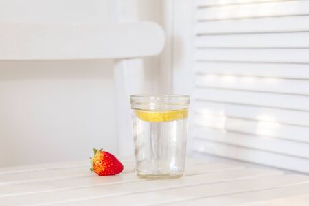 White background with a warm light. A glass of soda with a slice of lemon and a strawberry next to it in the center of the imageの写真素材