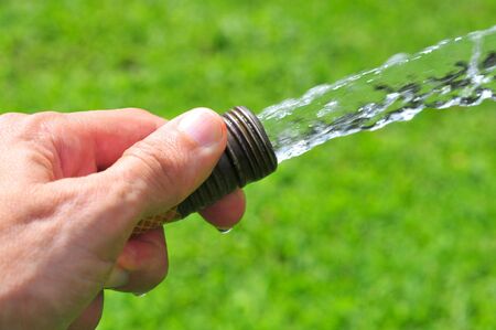 Hand holding a water hose on greenの写真素材