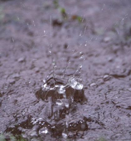 Close up view of a rain drop splashing into a small pool of rain waterの写真素材