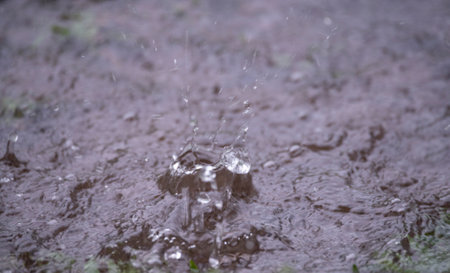Close up view of a rain drop splashing into a small pool of rain waterの写真素材
