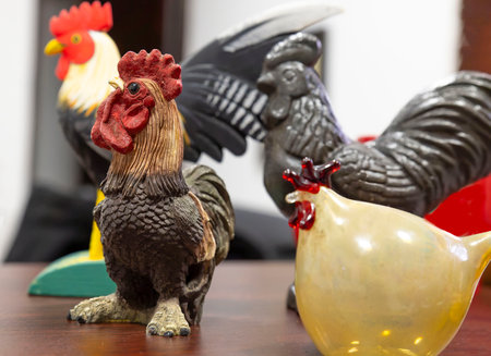 Photograph of a collection of rooster and hen figurines displayed on a wooden surface. The central focus is on a detailed, realistic rooster with vibrant red and brown tones.の写真素材