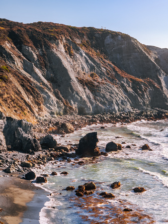Scenic coastline along the Pacific Coast near Big Sur, California. Ocean waves crashing down on sharp rocks of Willow Creek Beach with steep cliff in the warm light of setting sun at the background.の写真素材