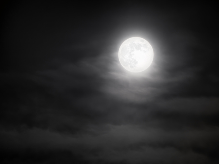 Full moon shining bright through the clouds at midnight. Dramatic night skyscape with the glowing moonlight, suitable for spiritual, mysterious or spooky concepts.の写真素材