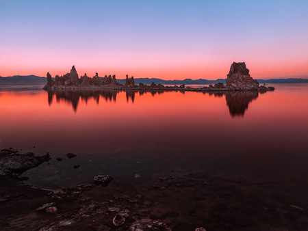 Beautiful serene lake after sunset. Long exposure photo taken at South Tufa Area of Mono Lake, California. Rock columns are reflecting in the water. Clear sky, blue hour colors with bright red glow.の写真素材