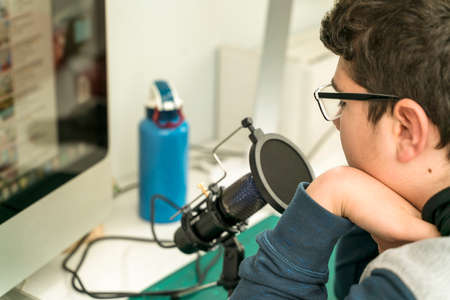A young Caucasian man looking at the computer in his room preparing a podcast or creating content for the Internet.の写真素材