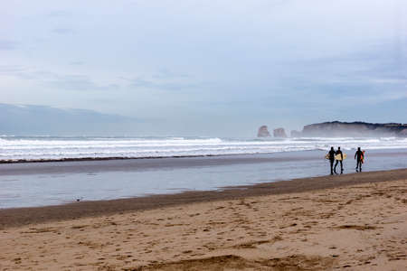 three surfers walk along the beach with their surfboards at sunset on a beach in northern Spain.の写真素材