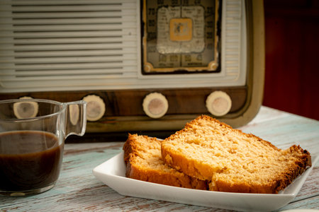 Portions of homemade sponge cake with black coffee on a vintage wooden table with a classic radio in...