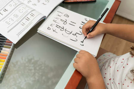 detail of a girl's hand with a black brush practicing calligraphy on a lined notebook. Learning the technique of letteringの写真素材