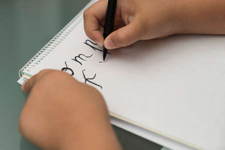 detail of a girl's hand with a black brush practicing calligraphy on a lined notebook. Learning the technique of letteringの写真素材