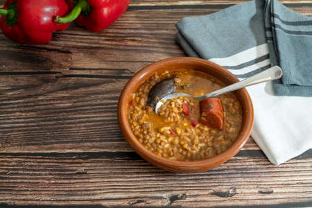 top view of a hand holding a spoon with lentils from a clay dish on a rustic wooden table with space for text. Healthy and traditional Spanish cuisine conceptの写真素材